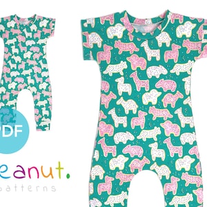May include: A teal blue short-sleeved jumpsuit with a white and pink animal cookie print. The print features a variety of animals, including giraffes, elephants, and hippos. The jumpsuit has a round neckline and a relaxed fit.
