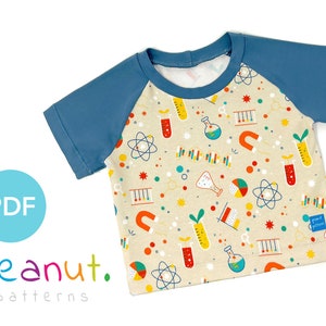 May include: A beige short-sleeved t-shirt with a blue raglan sleeve design. The t-shirt features a colorful science-themed pattern with beakers, atoms, magnets, and other science-related imagery. The text "peanut. patterns" is printed on the bottom left corner of the image.