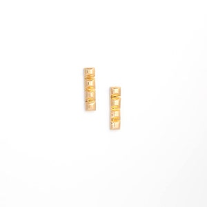 May include: A pair of gold-toned stud earrings with a geometric design. Each earring features three square-shaped elements.