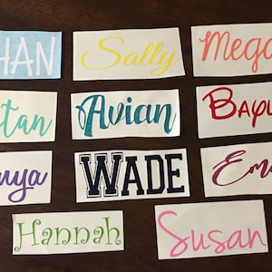 May include: A collection of 10 personalized name decals in various colors and fonts. The names include Ethan, Sally, Megan, Tristan, Avian, Bayley, Tonya, Wade, Emily, Hannah, and Susan.