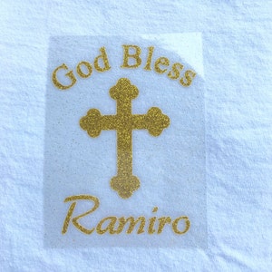 May include: Gold glitter iron-on with the text "God Bless Ramiro" and a gold glitter cross.