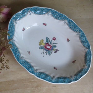 May include: A white oval serving dish with a blue and green scalloped edge. The dish features a floral design with pink, yellow, and green flowers.