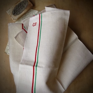 May include: A white linen tea towel with red and green stripes and the initials "GS" embroidered in the center.
