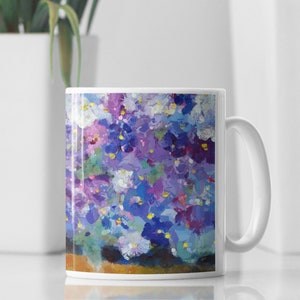 Pu&ograve; includere: Tazza in ceramica bianca con un design floreale colorato con fiori viola, blu e bianchi. La tazza ha un manico sul lato destro.