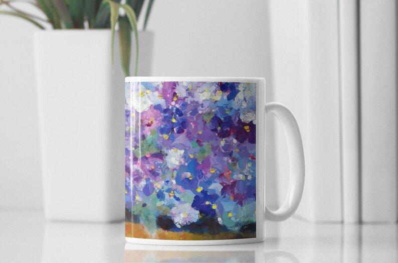 Pu&ograve; includere: Tazza in ceramica bianca con un design floreale colorato con fiori viola, blu e bianchi. La tazza ha un manico sul lato destro.