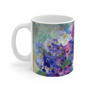 Pu&ograve; includere: Tazza in ceramica bianca con un design floreale astratto colorato in tonalit&agrave; di viola, blu e bianco. Il design ricorda un mazzo di fiori.