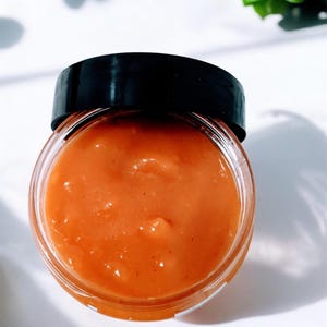 May include: A glass jar filled with a bright orange, smooth, and creamy-looking substance. The jar has a black lid.