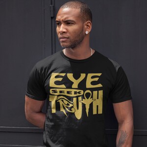 May include: A black t-shirt with a gold graphic design that reads "EYE SEEK TRUTH" with an Egyptian symbol in the middle of the word "TRUTH".