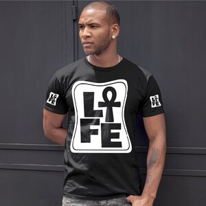 以下が含まれることがあります： 白い正方形のグラフィックが施された黒いTシャツ。グラフィックには「LIFE」という単語が書かれており、「I」の代わりにアンクのシンボルが使用されています。