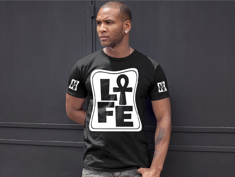 以下が含まれることがあります： 白い正方形のグラフィックが施された黒いTシャツ。グラフィックには「LIFE」という単語が書かれており、「I」の代わりにアンクのシンボルが使用されています。