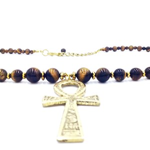 May include: A gold ankh pendant necklace with brown tiger's eye beads.