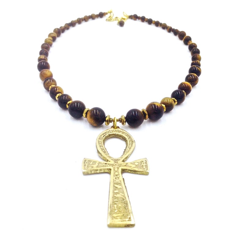 May include: A gold ankh pendant necklace with brown tiger's eye beads.