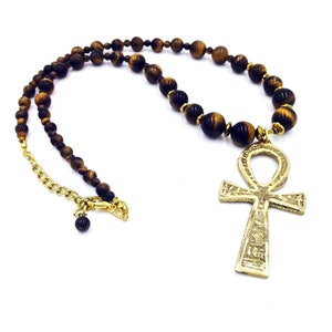 May include: A gold ankh pendant necklace with brown tiger's eye beads.