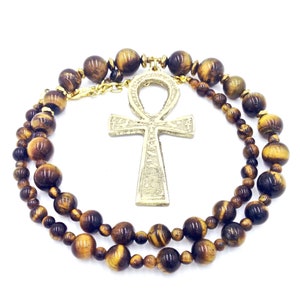May include: A gold Ankh pendant hangs from a double strand of tiger's eye beads.