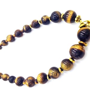 May include: A brown and gold tiger's eye beaded bracelet with gold accents. The bracelet is made of round beads and has a clasp closure.