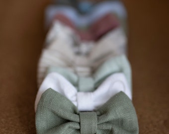 Può includere: Una fila di papillon di vari colori, tra cui bianco, azzurro, rosa e verde. Il papillon verde è a fuoco ed è fatto di tessuto di lino.