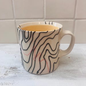 May include: A set of three ceramic mugs with a speckled, matte finish. The mugs are in shades of cream, light gray, and dark gray. Each mug has a simple, minimalist design, perfect for coffee or tea.