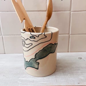 May include: A set of three ceramic mugs with a speckled, matte finish. The mugs are in shades of cream, light gray, and dark gray. Each mug has a simple, minimalist design, perfect for coffee or tea.