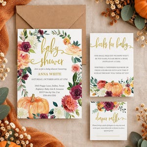 May include: A baby shower invitation set featuring a floral wreath with pumpkins, dahlias, and greenery. The text includes 'baby shower', 'books for baby', and 'diaper raffle' in gold script, with event details for Anna White on October 10th.
