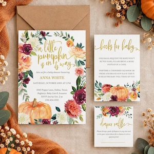 May include: A baby shower invitation set featuring a large card, a books for baby card, and a diaper raffle card. The cards have white backgrounds with gold cursive text and watercolor floral wreaths in orange, burgundy, and cream with pumpkins.