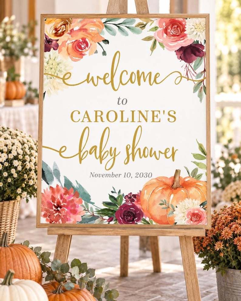 May include: A rectangular sign in a wooden frame featuring the text "welcome to CAROLINE'S baby shower November 10, 2030" in gold and black lettering, decorated with watercolor illustrations of orange pumpkins and various red and white flowers.