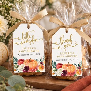 May include: Two clear plastic favor bags containing treats, each tied with a gold ribbon and a white rectangular tag. The tags feature gold text reading "little pumpkin" or "thank you," "LAUREN'S BABY SHOWER," and "November 30, 2030," with floral pumpkin art.