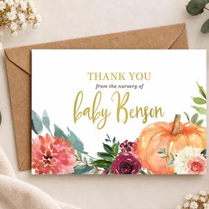 May include: A rectangular thank you card featuring the text THANK YOU from the nursery of baby Benson in gold and dark gray lettering. The design includes watercolor illustrations of a large orange pumpkin, red dahlias, and dark roses.