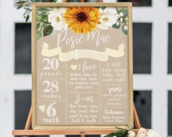 May include: A brown and white first birthday milestone poster with sunflowers and white flowers. The poster lists the child's name, Posie Mae, and details their age, weight, height, and number of teeth. The poster also includes a list of things the child loves, can do, and says.