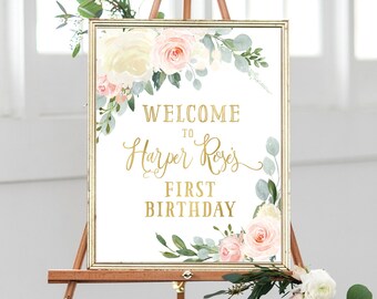 May include: A white sign with gold lettering and floral illustrations. The sign reads "Welcome to Harper Rose's First Birthday".