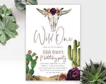 May include: A white birthday invitation card featuring a watercolor illustration of a cow skull adorned with dark red and orange flowers. The text reads Wild One, Join us to celebrate Adah Grace's 1st birthday party, Saturday, February 10, 2018.