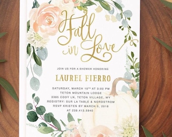 Puede incluir: Una tarjeta de invitación rectangular blanca con una corona floral de acuarela que incluye rosas color melocotón, flores blancas y hojas de eucalipto verdes. El texto en dorado dice Fall in Love, Laurel Fierro y los detalles del evento.