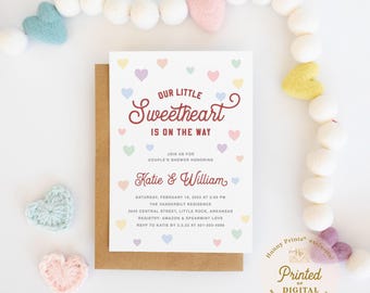 May include: A white baby shower invitation card with a brown envelope, featuring the text "OUR LITTLE Sweetheart IS ON THE WAY" and "Katie & William" in dark red, surrounded by small pastel-colored hearts in pink, blue, yellow, and green.