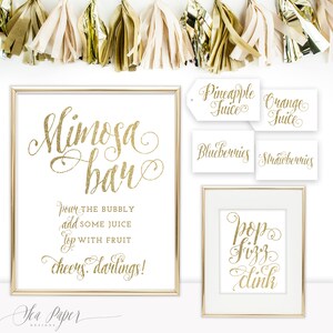 May include: Gold glitter printable signs for a mimosa bar. The signs read "Mimosa Bar", "Pour the bubbly, add some juice, top with fruit, cheers darlings!" and "Pop Fizz Clink". There are also smaller signs that read "Pineapple Juice", "Orange Juice", "Blueberries", and "Strawberries".