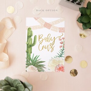 K&ouml;nnte beinhalten: Eine wei&szlig;e Karte mit einem rosa-wei&szlig;en Papierbanner oben. Die Karte hat einen gr&uuml;nen Kaktus, wei&szlig;e und rosa Blumen und gr&uuml;ne Bl&auml;tter. Der Text "Baby Cruz" ist in goldener Schrift geschrieben.