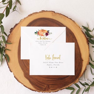 Op de afbeelding: Twee witte enveloppen met gouden letters. De bovenste envelop heeft een aquarel-illustratie van een pompoen, bladeren en bloemen. De tekst op de bovenste envelop luidt "the fallens" en bevat een adres. De onderste envelop heeft de tekst "Katie Lamont" en bevat een adres.