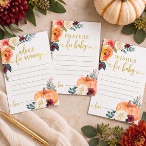 May include: Three rectangular white paper cards featuring watercolor floral arrangements with orange, burgundy, and white flowers, green leaves, and orange pumpkins. The cards have gold text reading Advice for mommy, Prayers for baby, and Wishes for baby.