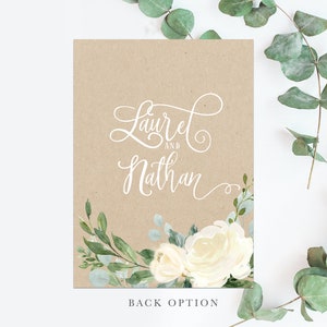 K&ouml;nnte beinhalten: Eine Hochzeitseinladung aus Kraftpapier mit wei&szlig;er Kalligrafie, die "Laurel und Nathan" lautet, und einem Aquarell-Blumendesign mit wei&szlig;en Rosen und gr&uuml;nen Bl&auml;ttern.