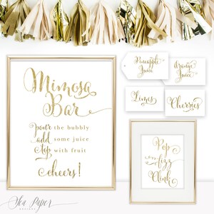 May include: Gold glitter sign with the text "Mimosa Bar" and instructions to "pour the bubbly, add some juice, top with fruit, cheers!"  Four smaller signs with the text "Pineapple Juice", "Orange Juice", "Limes", and "Cherries". A sign with the text "Pop Fizz Clink".