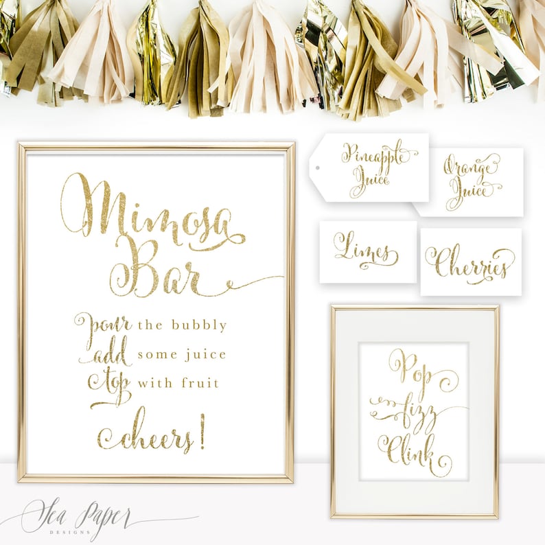 May include: Gold glitter sign with the text "Mimosa Bar" and instructions to "pour the bubbly, add some juice, top with fruit, cheers!"  Four smaller signs with the text "Pineapple Juice", "Orange Juice", "Limes", and "Cherries". A sign with the text "Pop Fizz Clink".