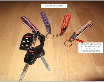 Puede incluir: Una colección de llaveros y cordones de identificación en varios colores, incluyendo negro, rosa, morado, naranja y un patrón de arcoíris. Cada cordón presenta un diseño trenzado y un anillo metálico para sujetar llaves. El texto dice: KEYCHAIN/ID LANYARD.