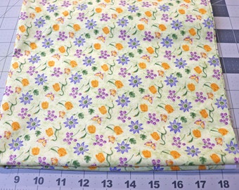 May include: A folded piece of light green fabric featuring a repeating pattern of orange tulips, purple star-shaped flowers, small clusters of tiny purple blossoms, and orange butterflies. A ruler is visible at the bottom showing 19 inches.