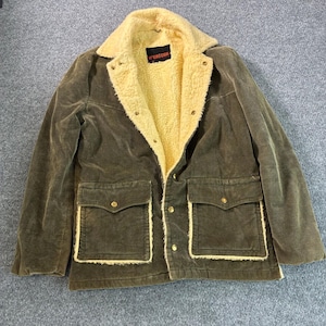 May include: An olive green corduroy jacket featuring a cream-colored sherpa lining and collar. The jacket includes two front flap pockets with gold-tone snap buttons, a front snap button closure, and a black McGregor brand label at the neck.