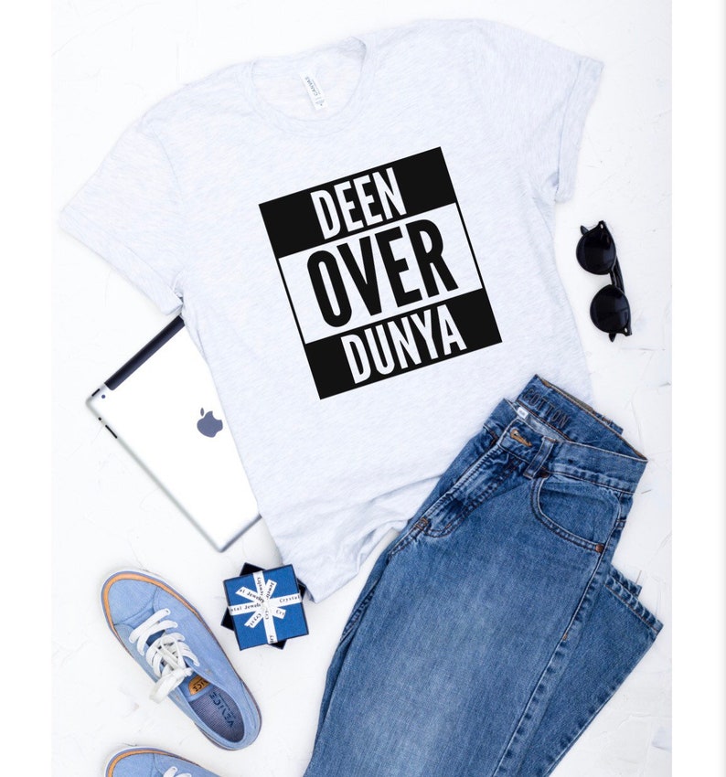 May include: A white t-shirt with a black square graphic that says "DEEN OVER DUNYA" in white letters. The shirt is paired with blue jeans and blue sneakers.