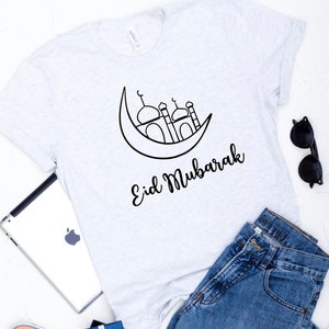May include: A white t-shirt with a black outline of a crescent moon and a mosque with the text "Eid Mubarak" underneath.
