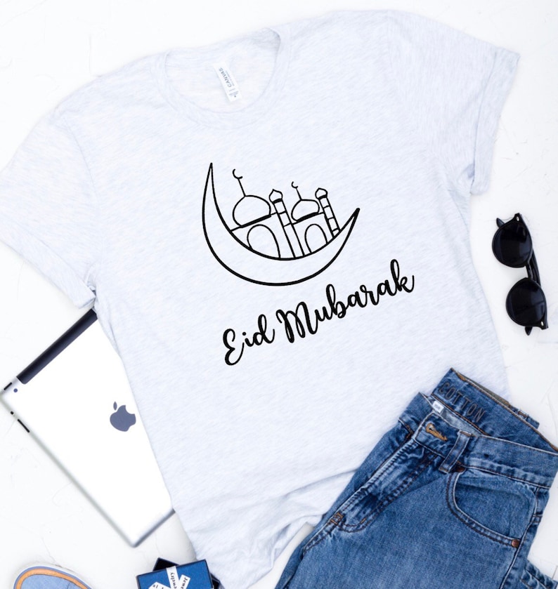 May include: A white t-shirt with a black outline of a crescent moon and a mosque with the text "Eid Mubarak" underneath.