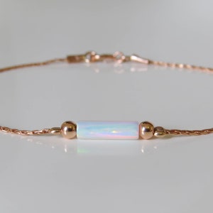 May include: A delicate rose gold chain bracelet with a white opal bar charm. The bracelet is simple and elegant, perfect for everyday wear.