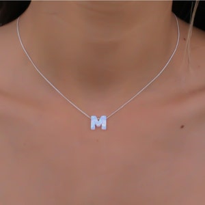 May include: A silver chain necklace with a white letter M pendant.