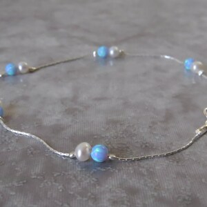 Pu&ograve; includere: Un braccialetto per caviglia in catena d'argento con perline di opale blu e perle bianche alternate.