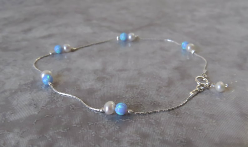 Pu&ograve; includere: Un braccialetto per caviglia in catena d'argento con perline di opale blu e perle bianche alternate.
