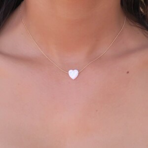 May include: A delicate gold chain necklace with a white heart pendant.